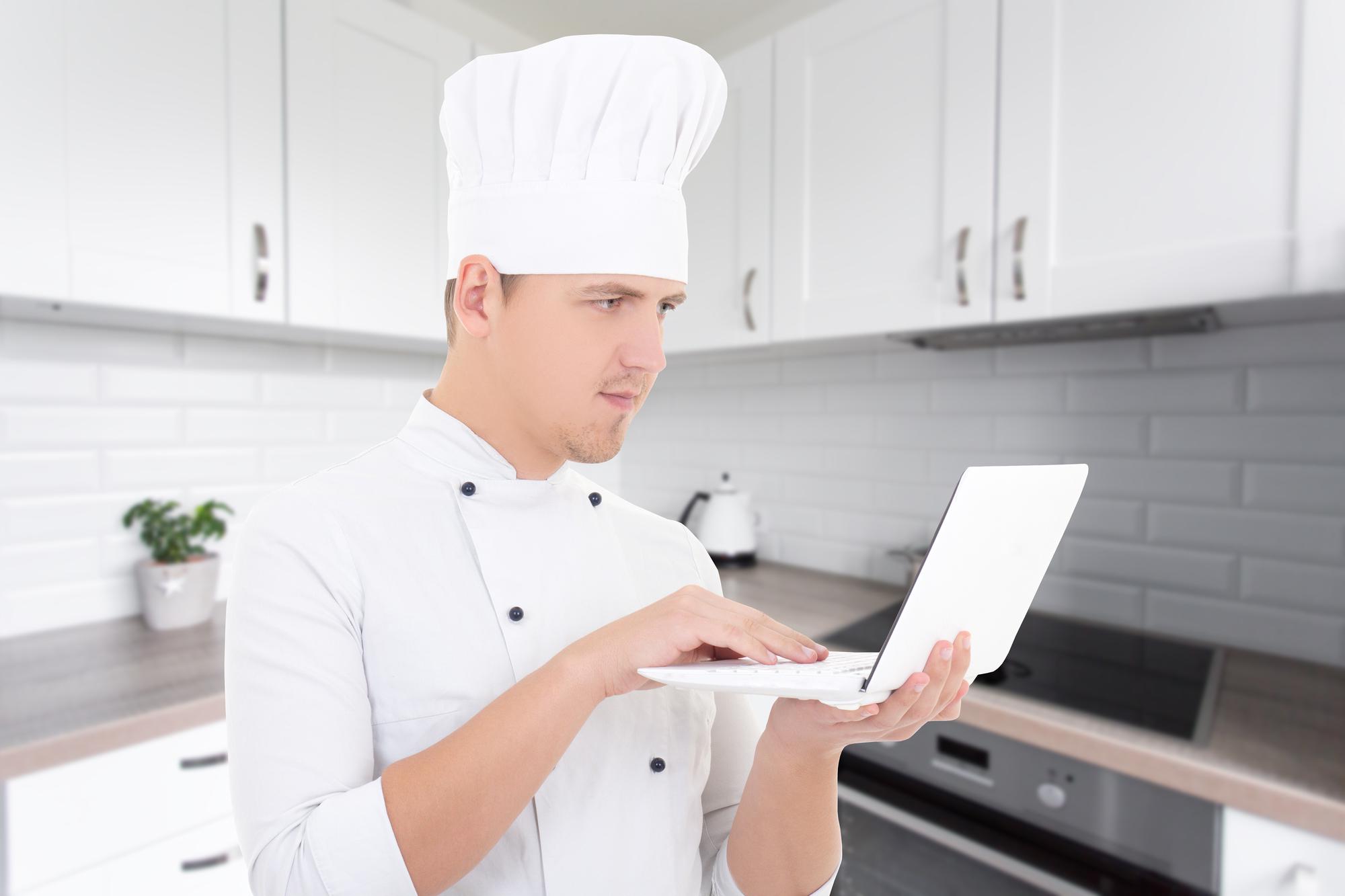 Chef al lavoro in cucina tecnologica con laptop